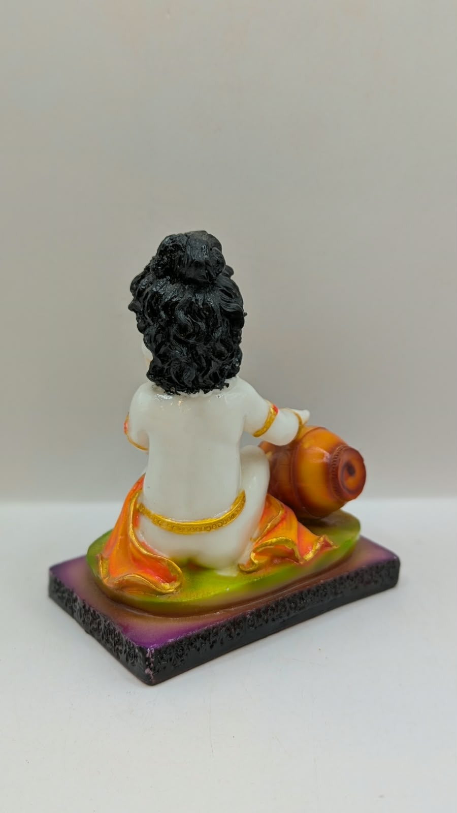 White baby Krishna statue eating butter, green base, back view