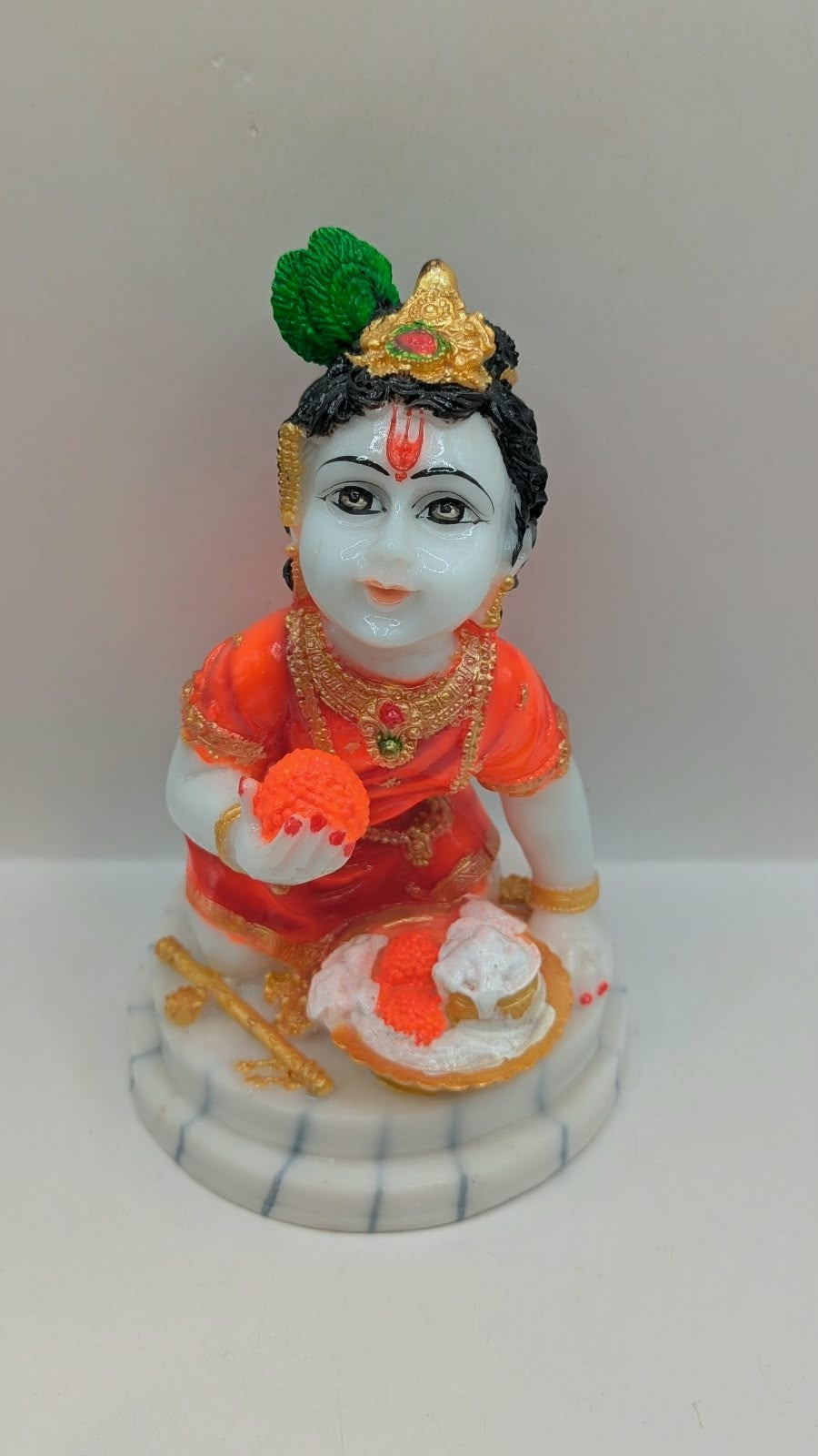 Bal Gopal statue in orange holding laddoo, front view