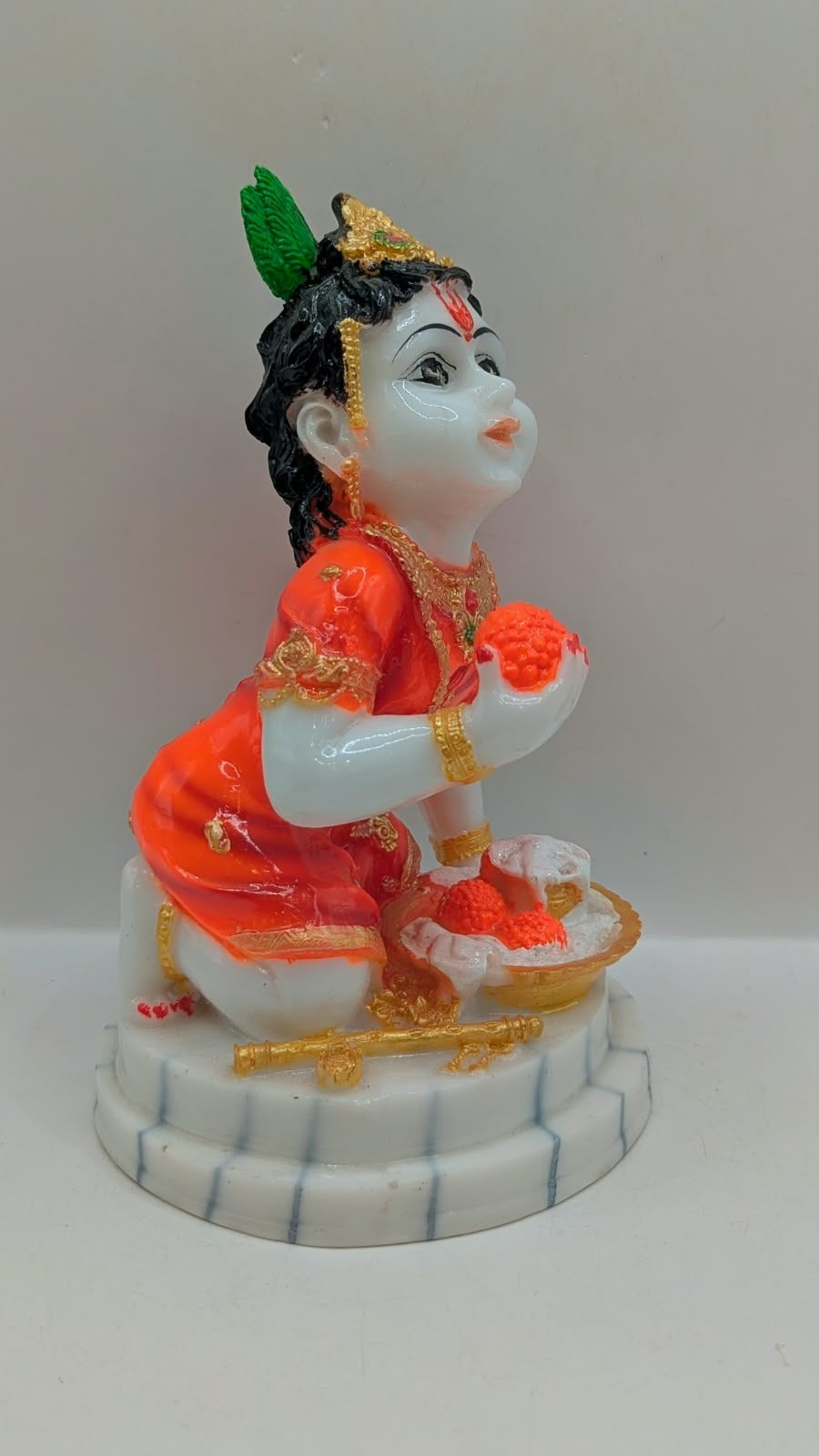 Bal Gopal statue in orange holding laddoo, side view