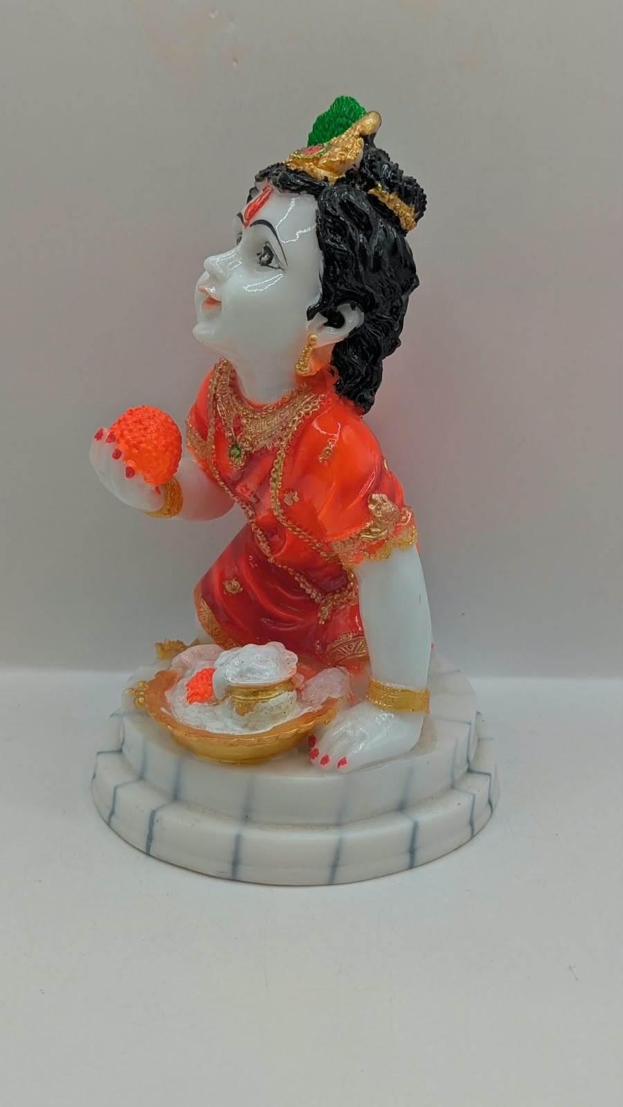 Bal Gopal statue in orange holding laddoo, other side view