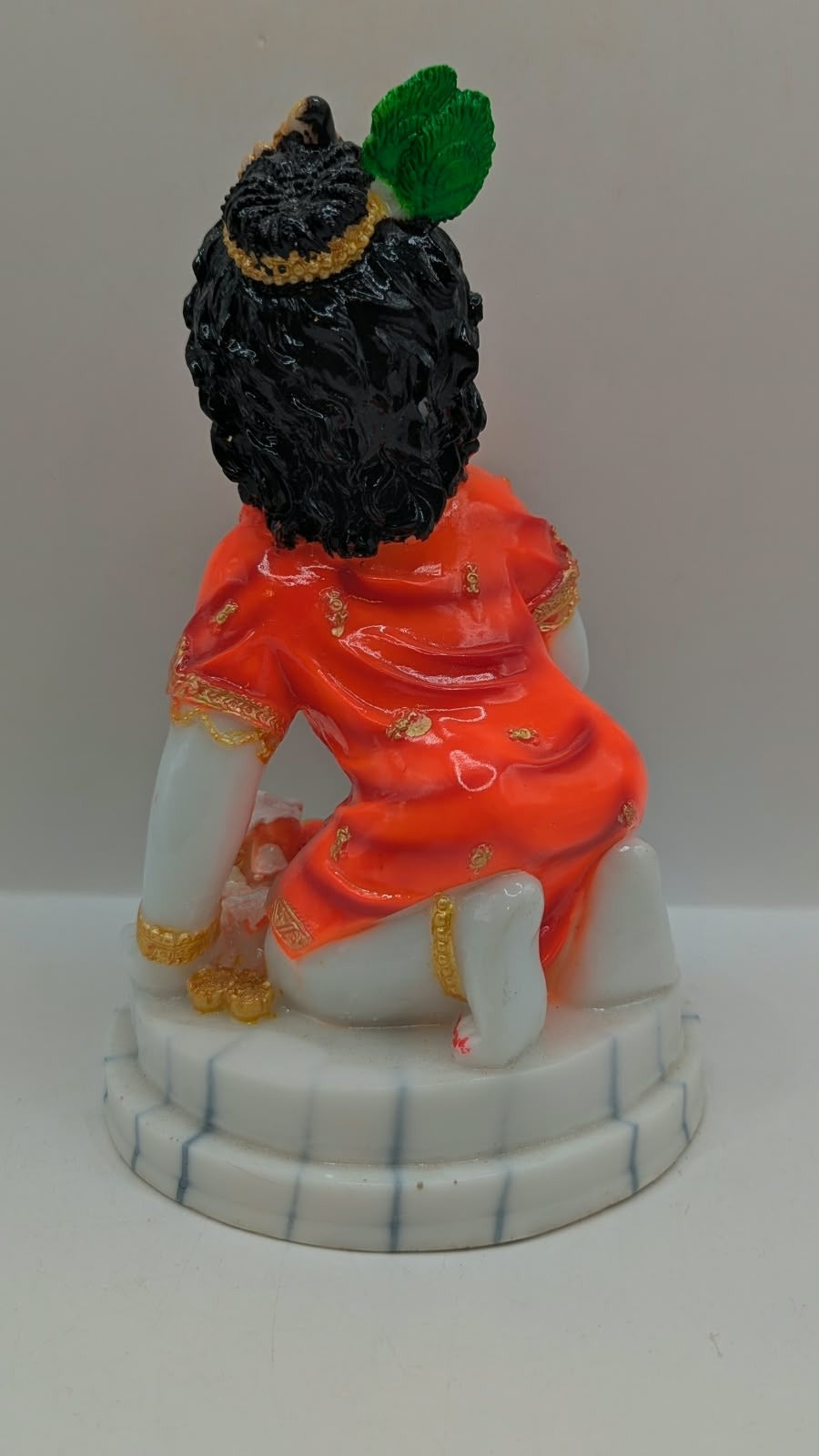 Bal Gopal statue in orange holding laddoo, back view
