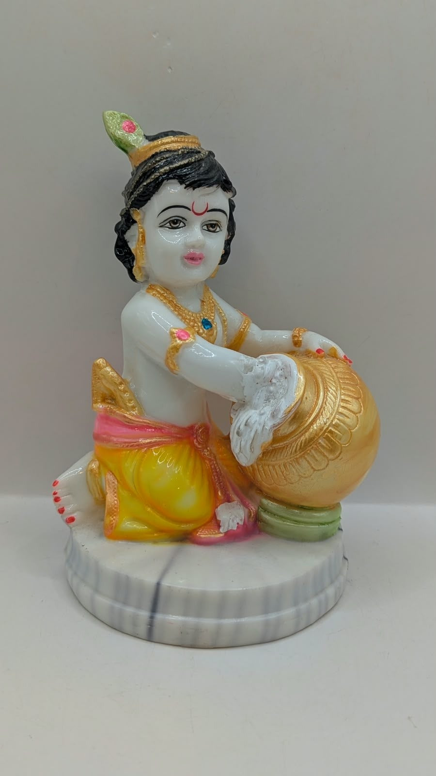 Baby Krishna statue hugging gold pot, side view