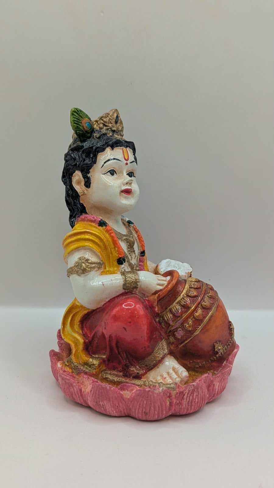 Baby Krishna statue in red dhoti on pink lotus, side view